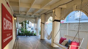 A covered outdoor area with a hammock swing, a red sign on the wall, and a paved floor.
