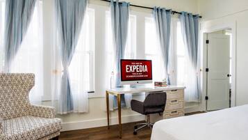 A bedroom with a bed, a desk with a computer, a chair, and a patterned armchair.