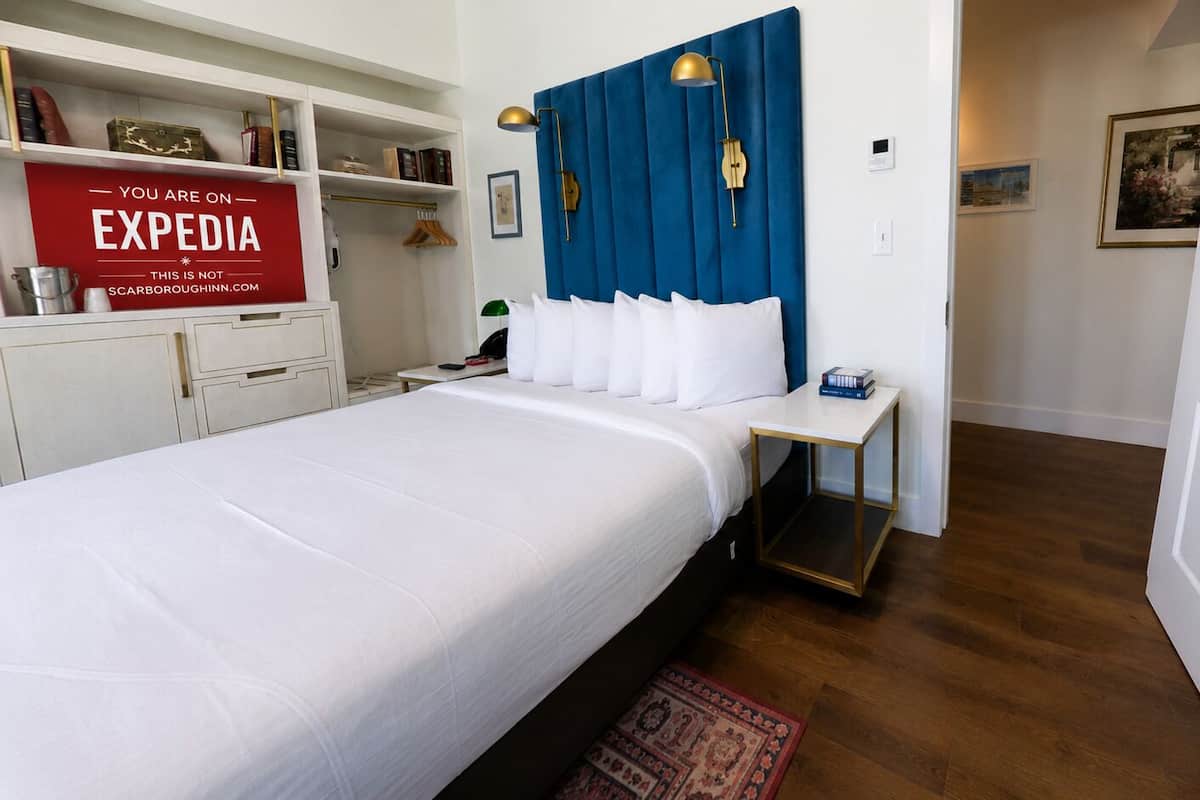 Une chambre d’hôtel avec un grand lit, une table de chevet, une tête de lit bleue et un panneau rouge accroché au mur.