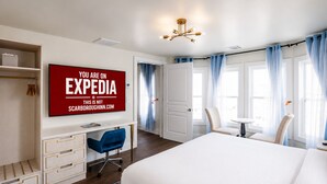 A hotel room with a large bed, a desk with a chair, a television, and a wardrobe.