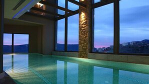 An indoor swimming pool with a stone pillar and large windows offering a view of a mountainous landscape.
