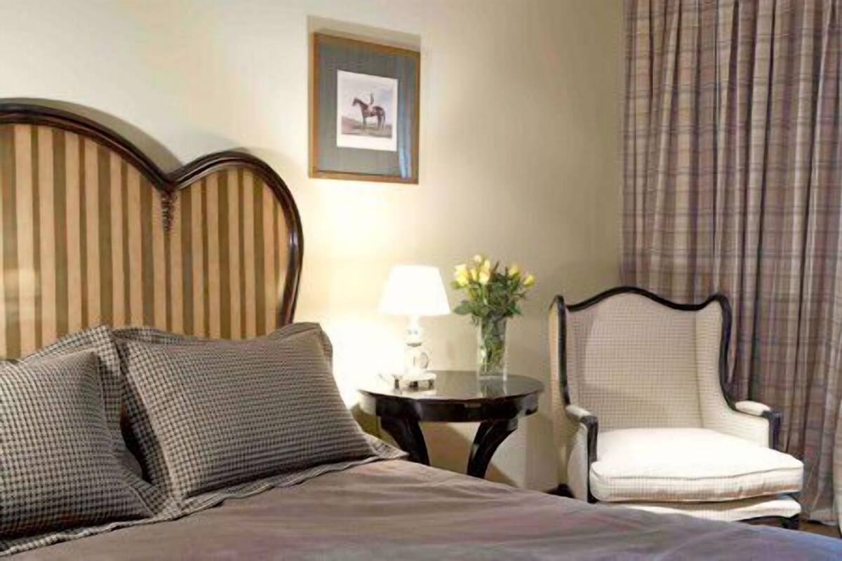 Ein Hotelzimmer mit Bett, einem Sessel, einem Tisch mit Lampe und einem gerahmten Bild an der Wand.