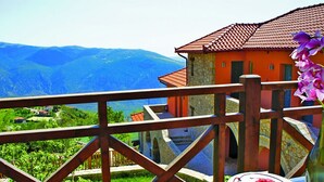 A balcony with a view of mountains, a stone building with a tiled roof, and a plate of strawberries.