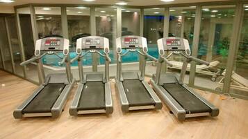 Cuatro cintas de correr en un gimnasio con una pared de vidrio y vistas a una piscina.