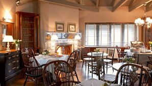 A dining area with wooden chairs and tables, a fireplace, and a large window with blinds.
