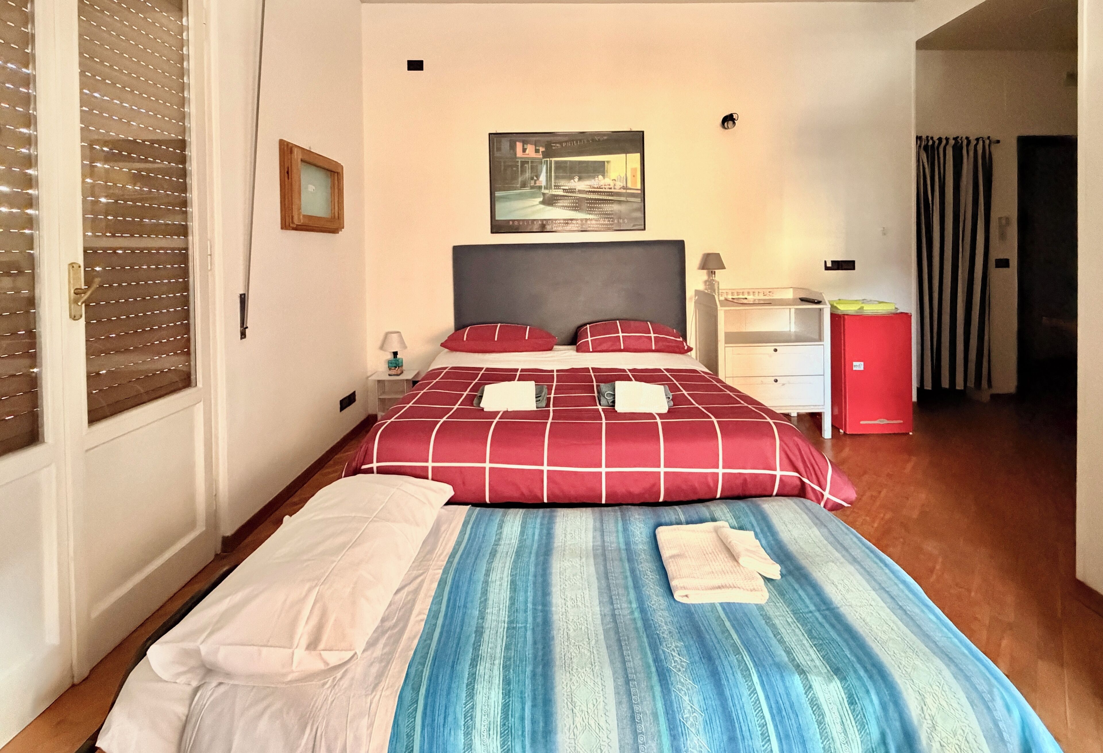 A hotel room with a bed, a nightstand, a red cabinet, and a framed picture on the wall.