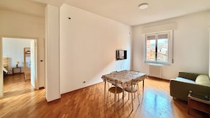 Amplia sala de estar con piso de madera, una mesa de comedor con sillas, un sofá y un televisor montado en la pared.