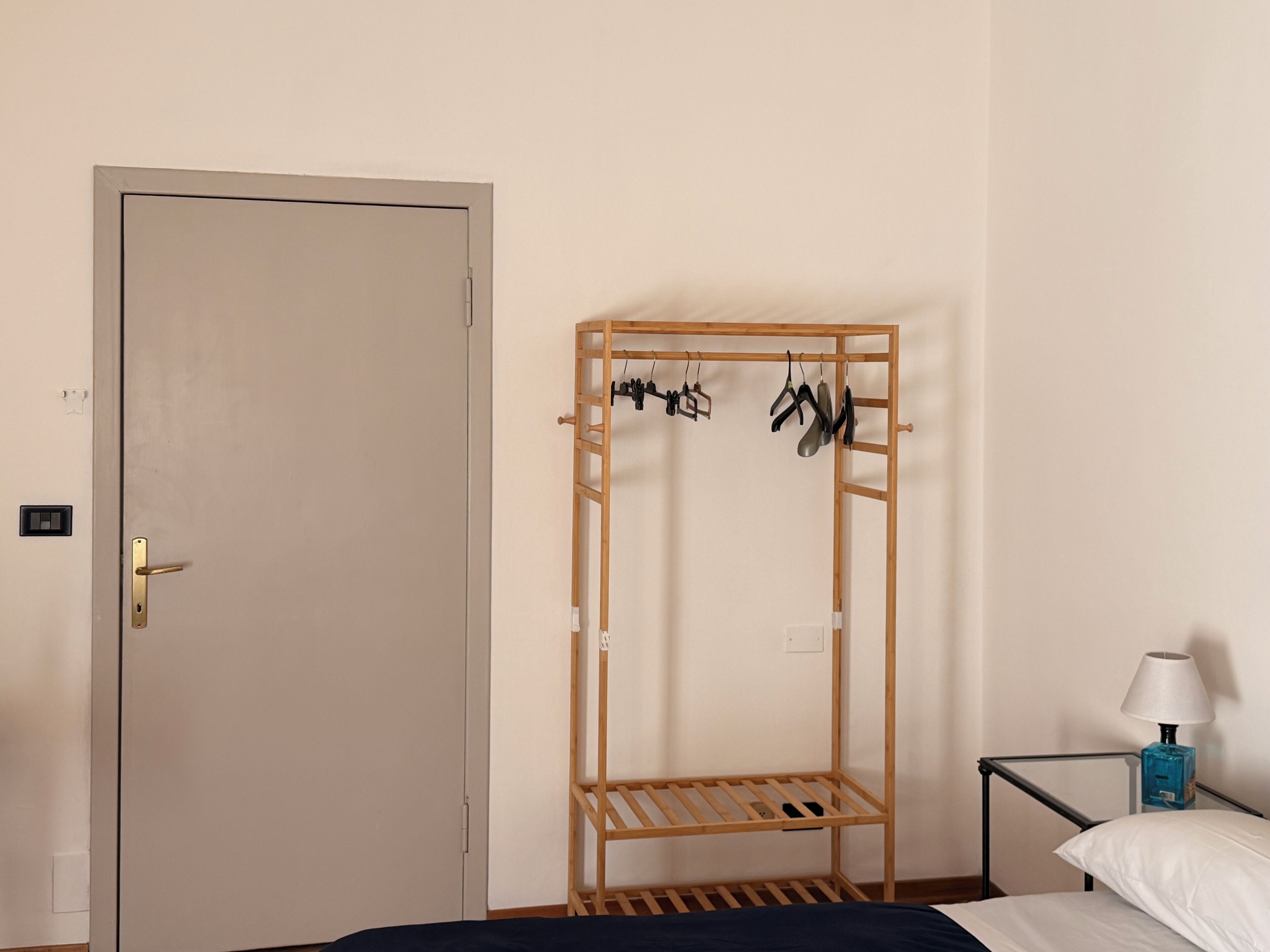 Un dormitorio con un armario de madera, una estructura metálica para la cama, una mesita de noche con una lámpara y un tendedero adosado a la pared.