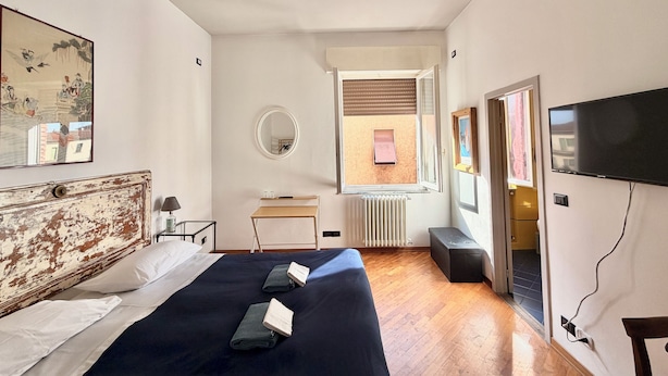 Un dormitorio con una cama, ventilador de techo, escritorio, silla, televisor y ventana con persianas.