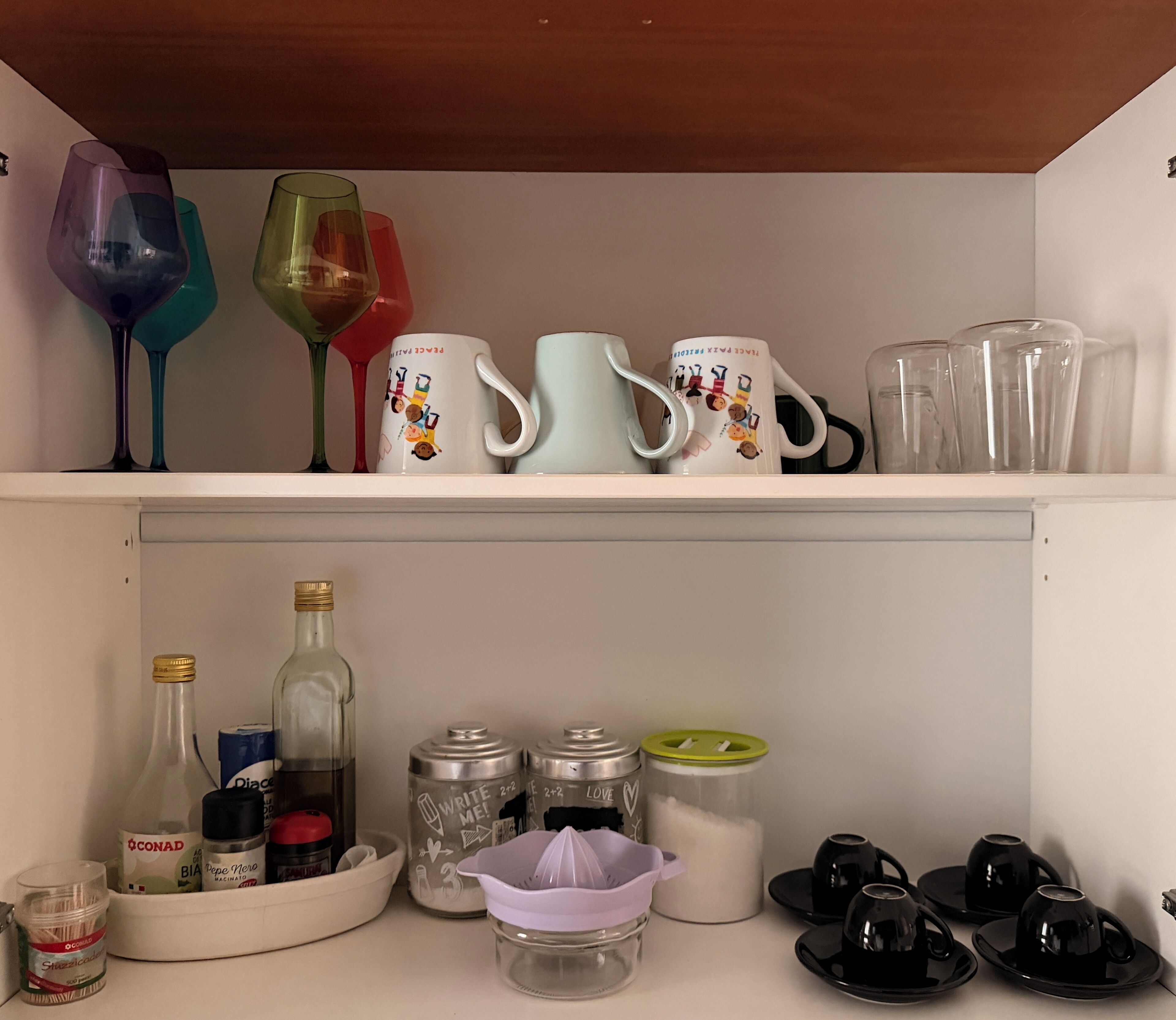 A kitchen shelf with various glassware, including wine glasses, a teapot, and storage containers.