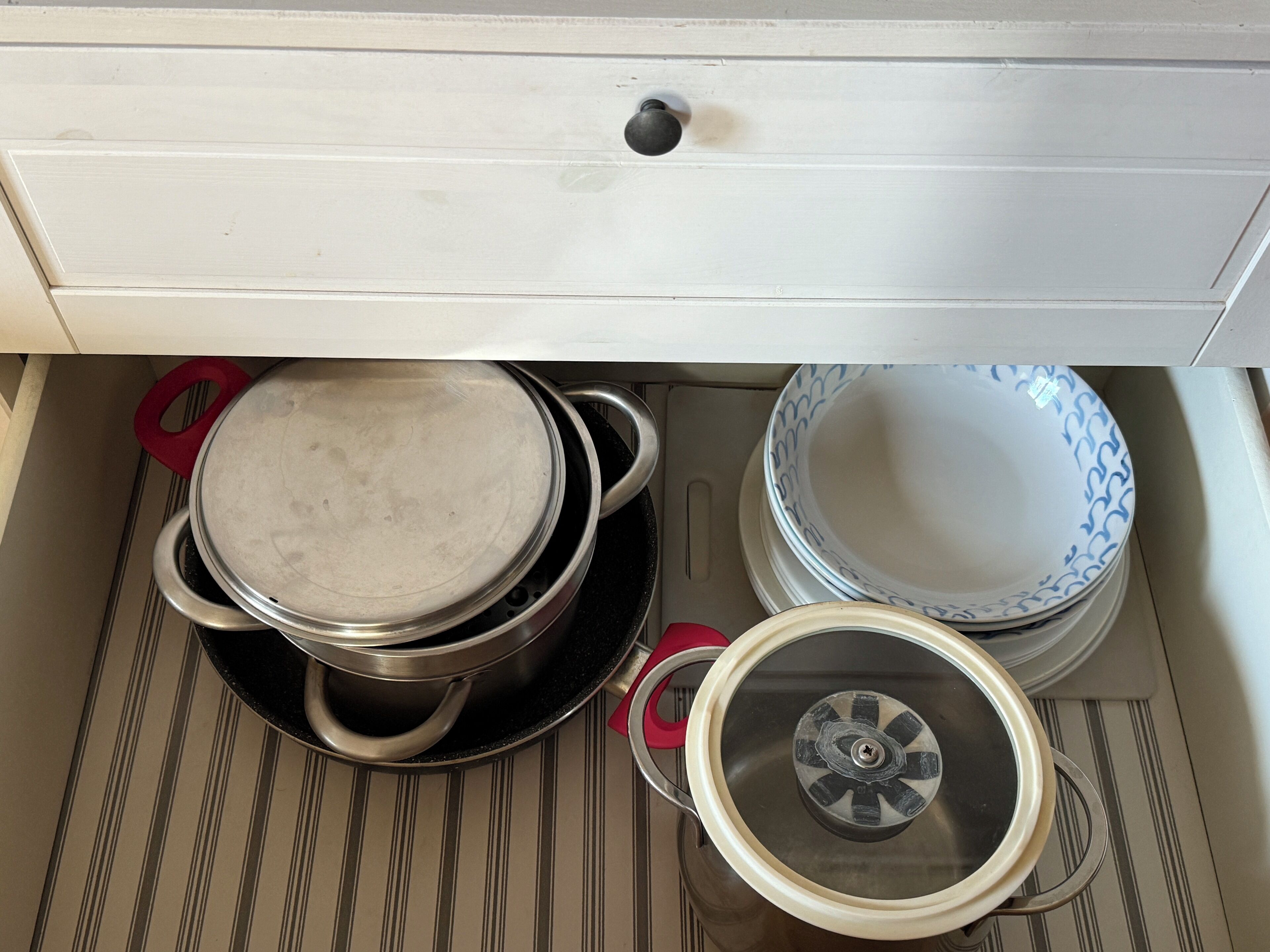 A kitchen drawer with pots and pans, a white cabinet, and a striped floor.