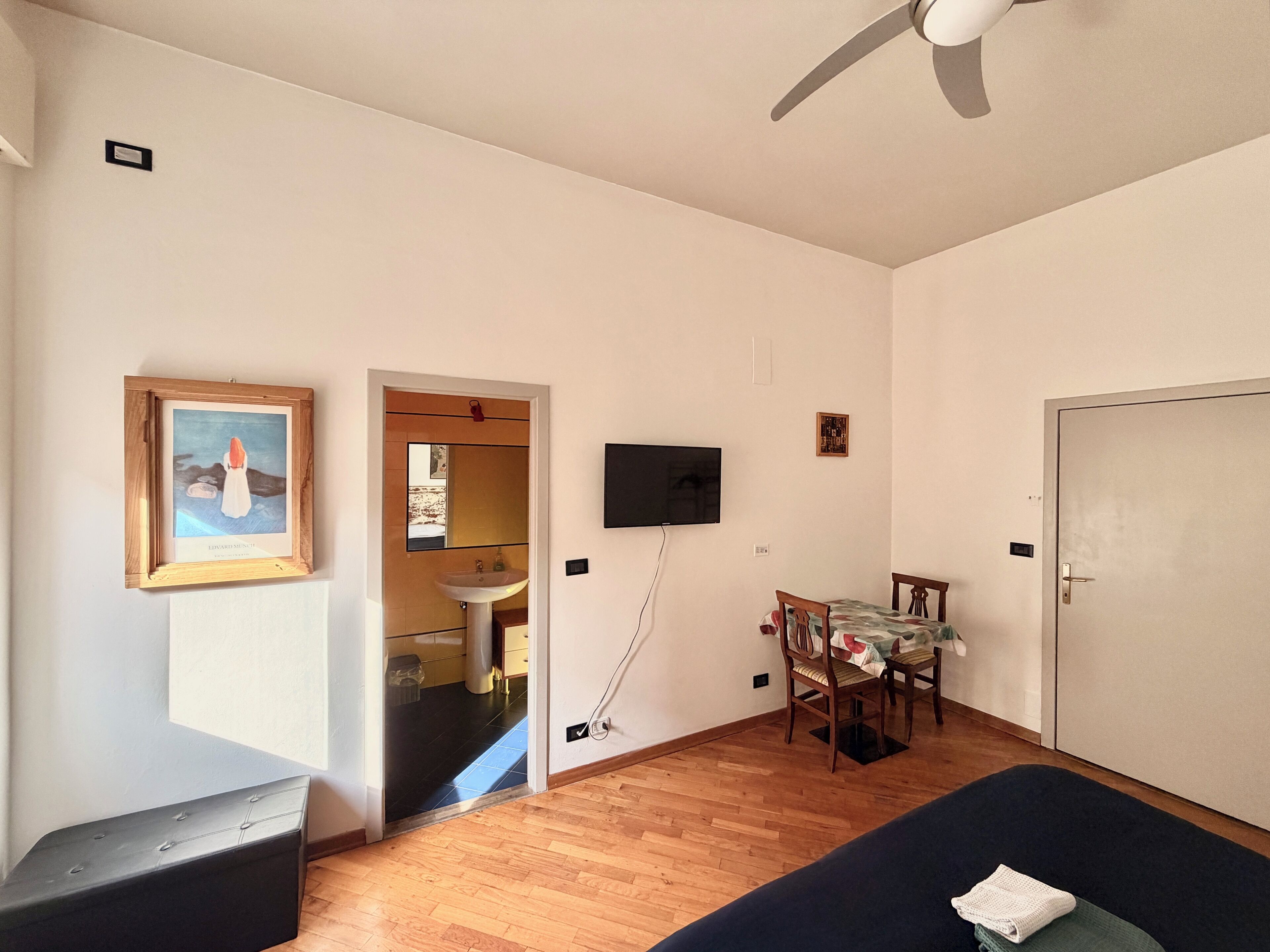 Een kamer met een bed, bureau, stoel, televisie en een deur.