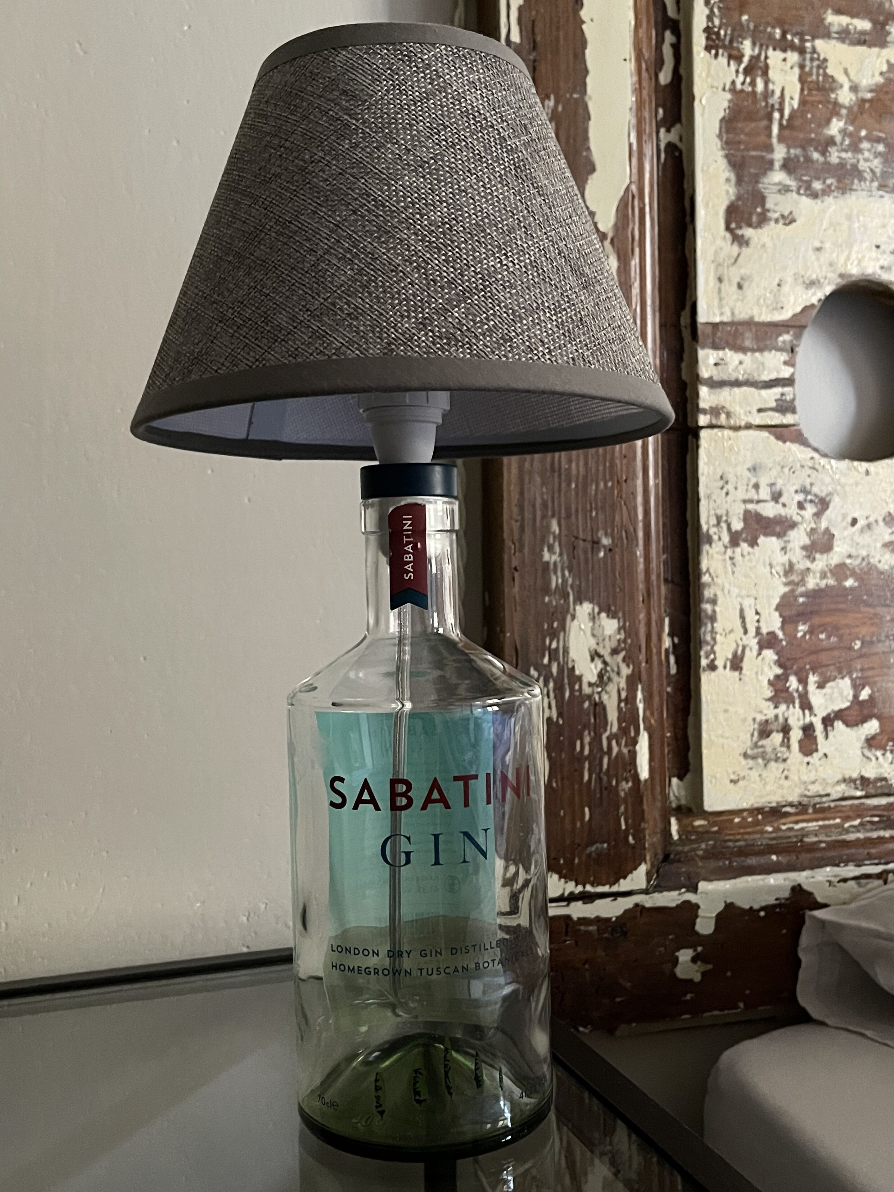 Een fles Sabatini Gin op een tafel met een lantaarnkap met structuur.
