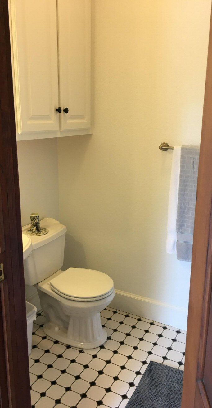 A bathroom with a toilet, a white cabinet, and a tiled floor.