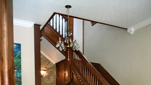 A wooden staircase with a chandelier, a bench with cushions, and a rug in a room with wooden floors and a stone wall. - Three Danes Inn (Fort Worth)