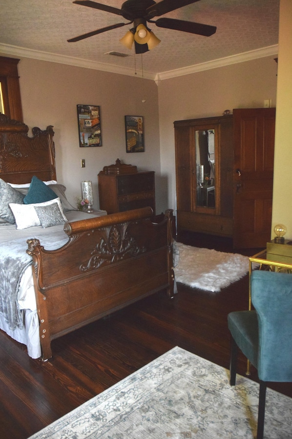 A bedroom with a wooden bed, a chair, a mirror, and a ceiling fan. - Three Danes Inn (Fort Worth)