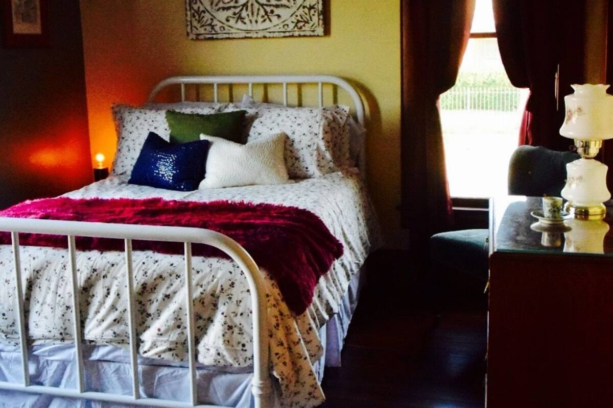 A bedroom with a bed, a ceiling fan, a nightstand, a lamp, and a window with curtains.