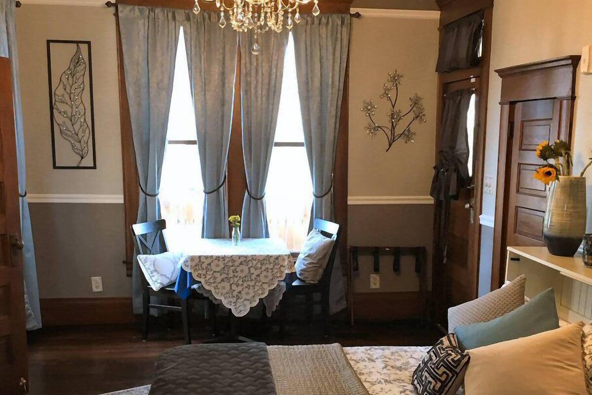 A bedroom with a large bed, a chandelier, a dining table with chairs, and a vase with flowers.