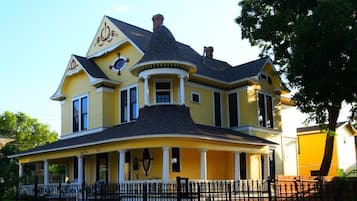 Stunning two-story house with a gabled roof and wrap-around porch, set amidst a tree-lined landscape.