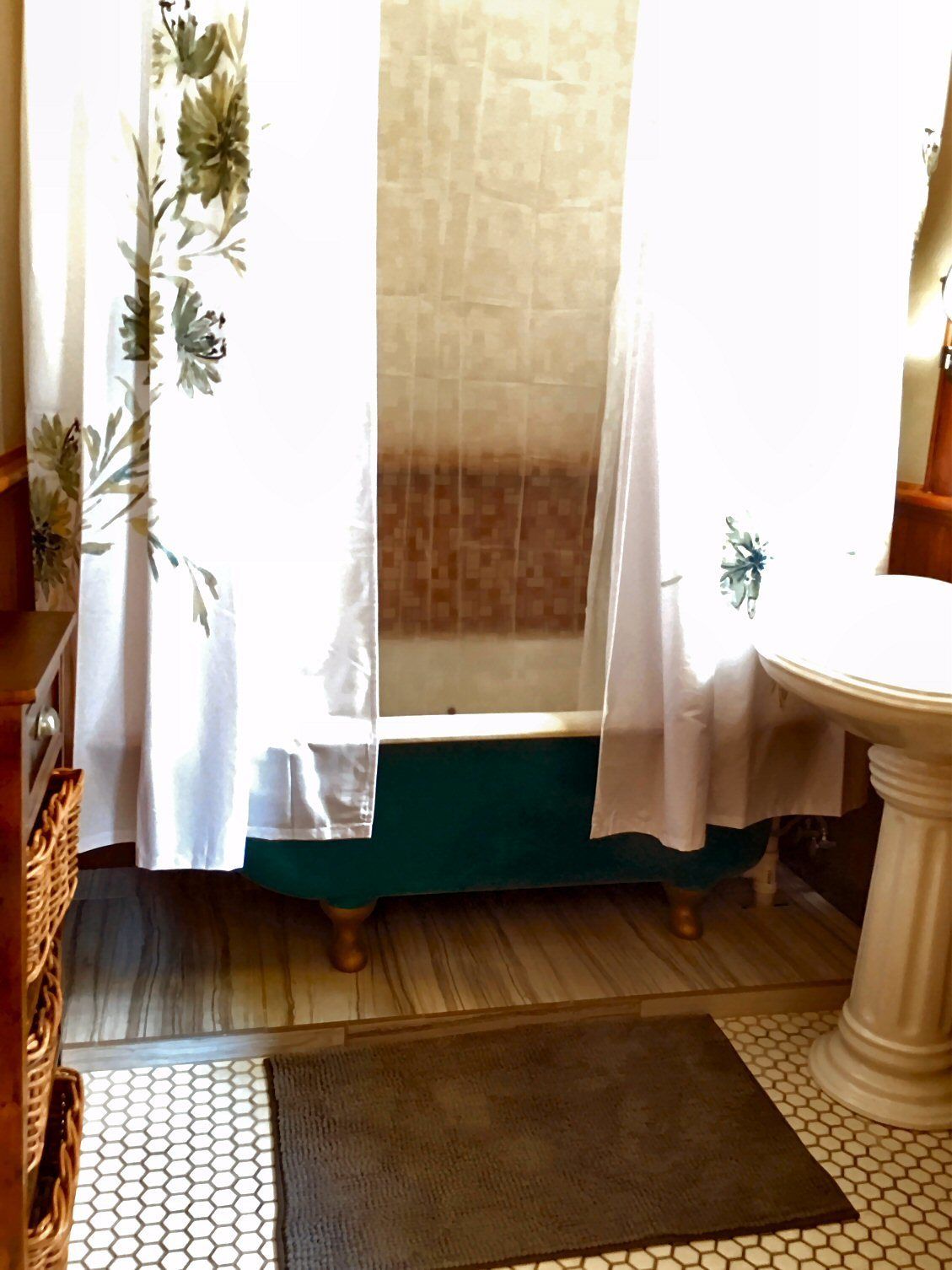 A bathroom with a bathtub, a sink, and a window with curtains.