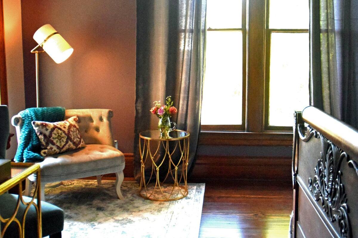 A room with a sofa, a small round table with a vase, a lamp, and a window with curtains.