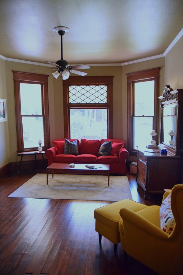 Una sala de estar con un sofá rojo, un sillón amarillo, una mesa de centro de madera y un ventilador de techo.