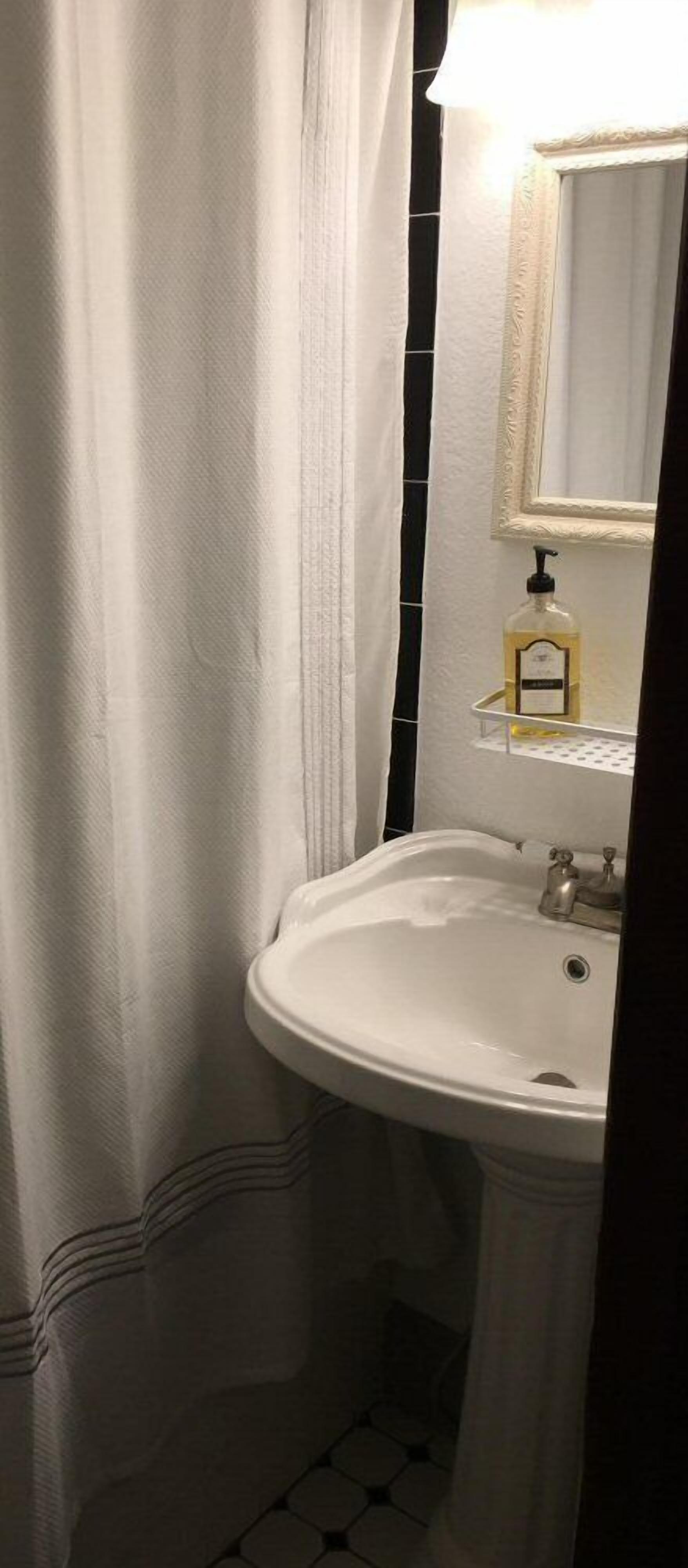 A bathroom with a white sink, a mirror, and a bottle of hand soap on a shelf.