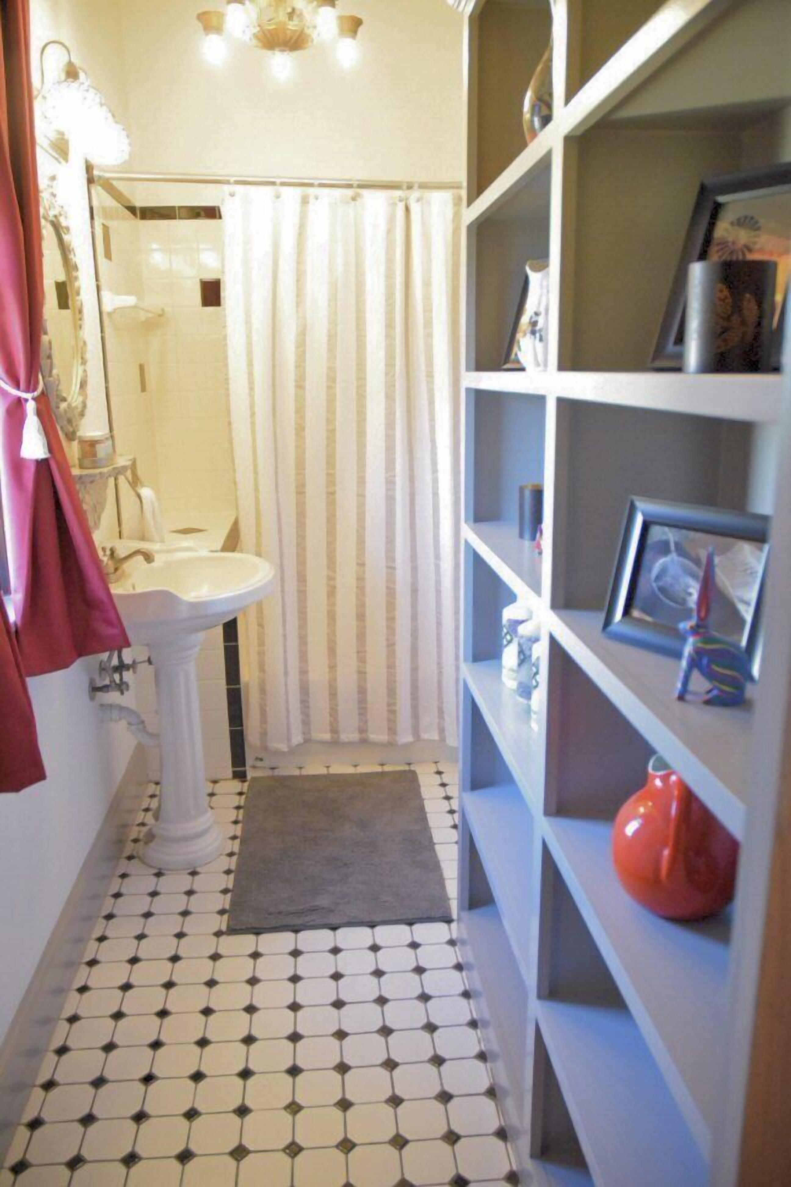 A bathroom with a white pedestal sink, a shower with a striped curtain, and a tiled floor.