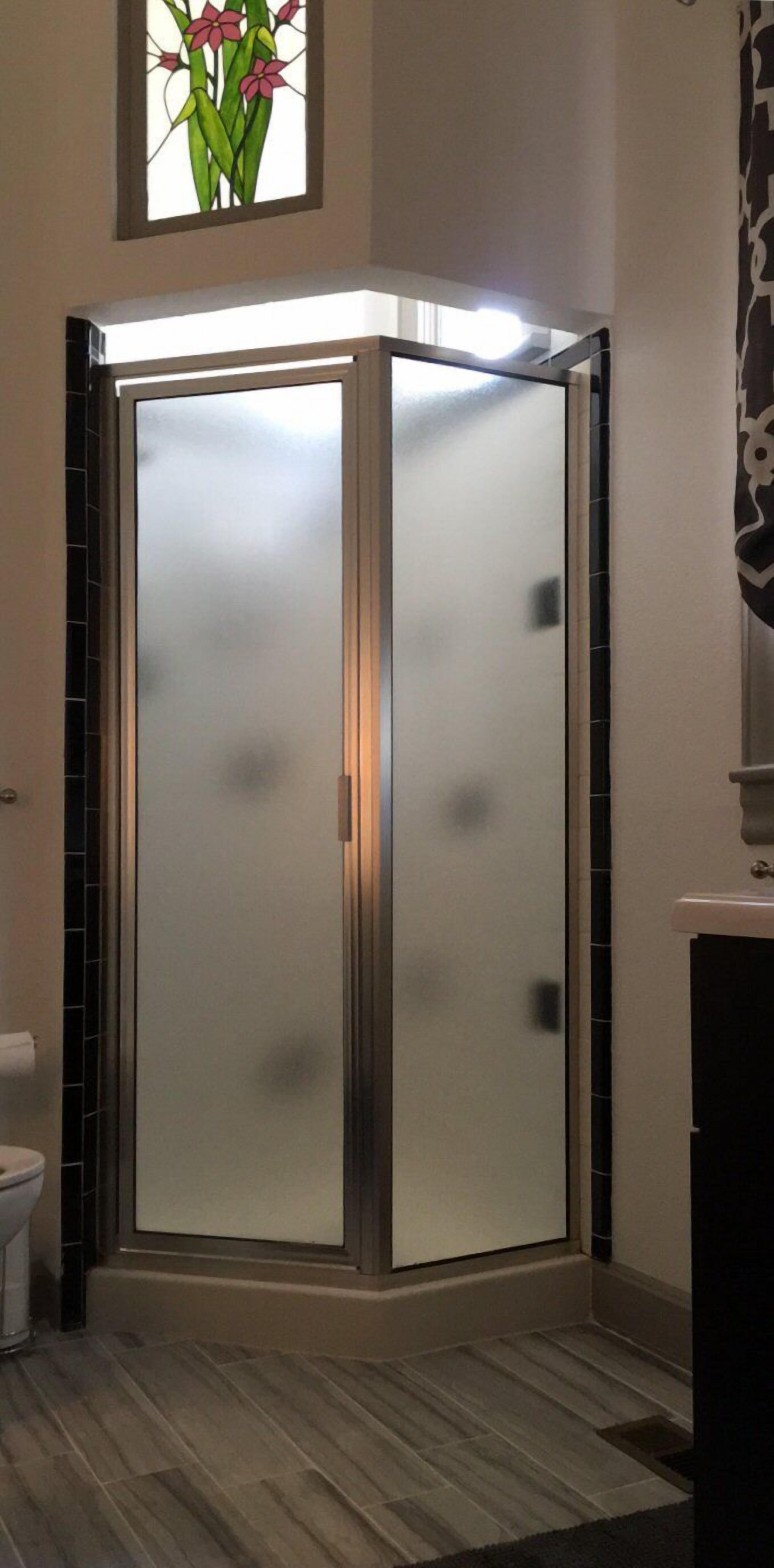 A bathroom with a glass-enclosed shower, a toilet, and a decorative stained glass window above the shower.