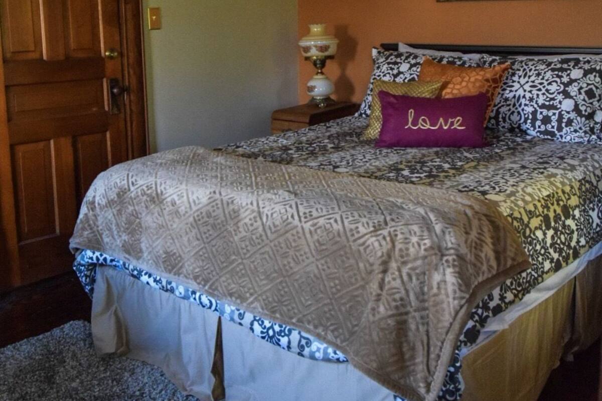 A bedroom with a bed, a ceiling fan, a lamp, and a painting on the wall.