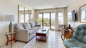 A modern living room with a sofa, a glass coffee table, a wicker chair, and a television. - Kihei Akahi (Kihei)