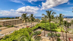 A hotel with a parking lot, palm trees, and a view of the ocean. - Kihei Akahi (Kihei)