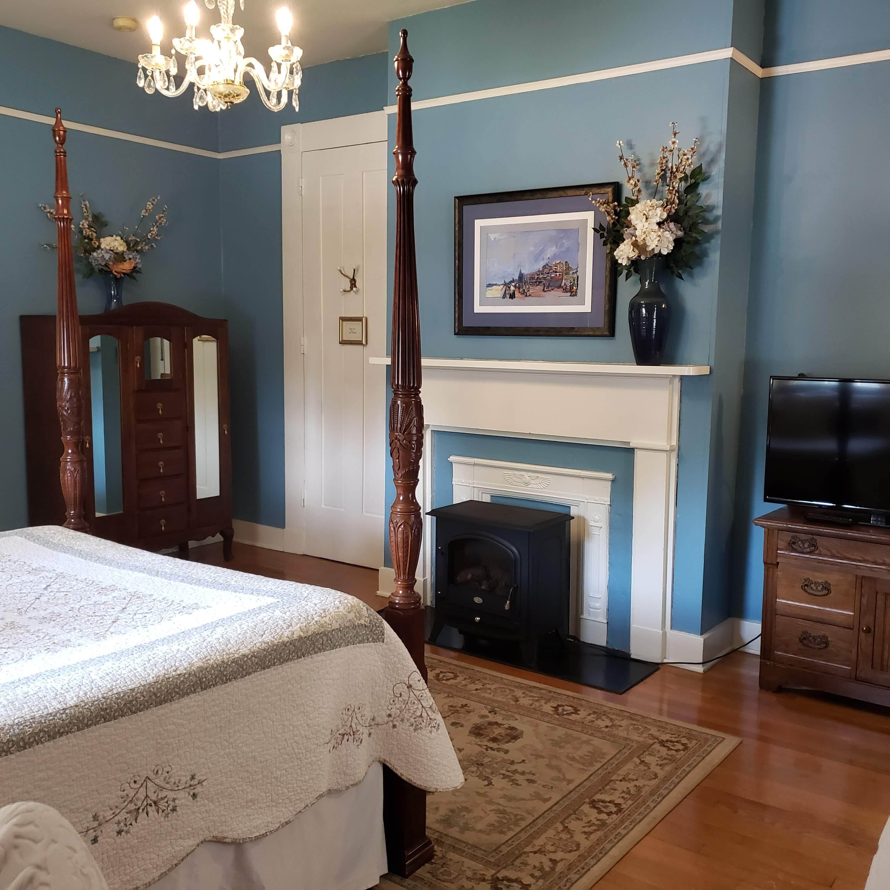 A bedroom with a four-poster bed, a fireplace, a television, and a dresser.