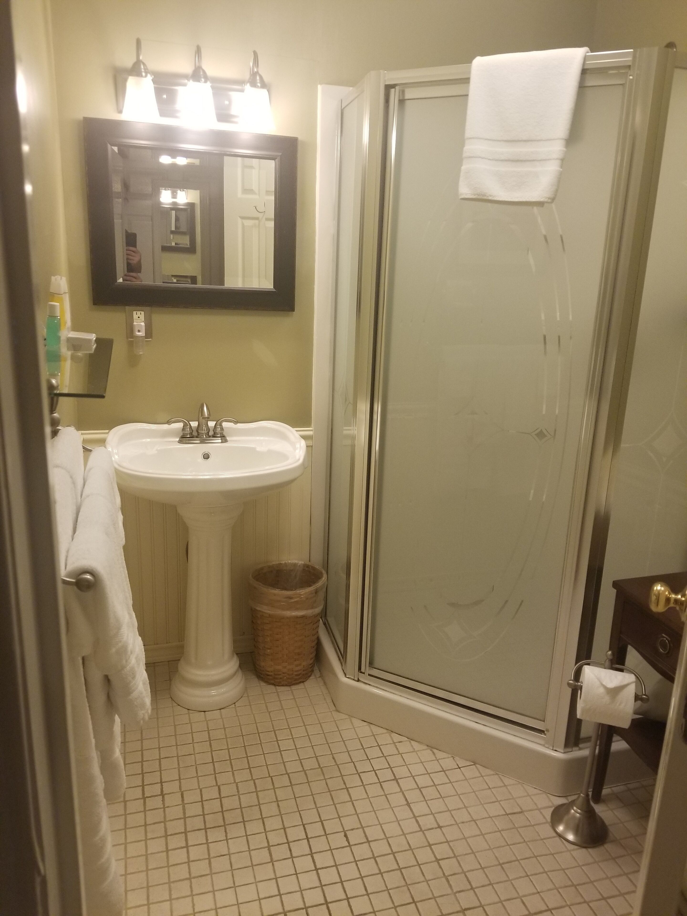 A bathroom with a pedestal sink, a glass shower enclosure, and a mirror above the sink.