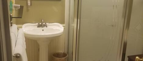 A bathroom with a pedestal sink, a glass shower enclosure, and a mirror above the sink.