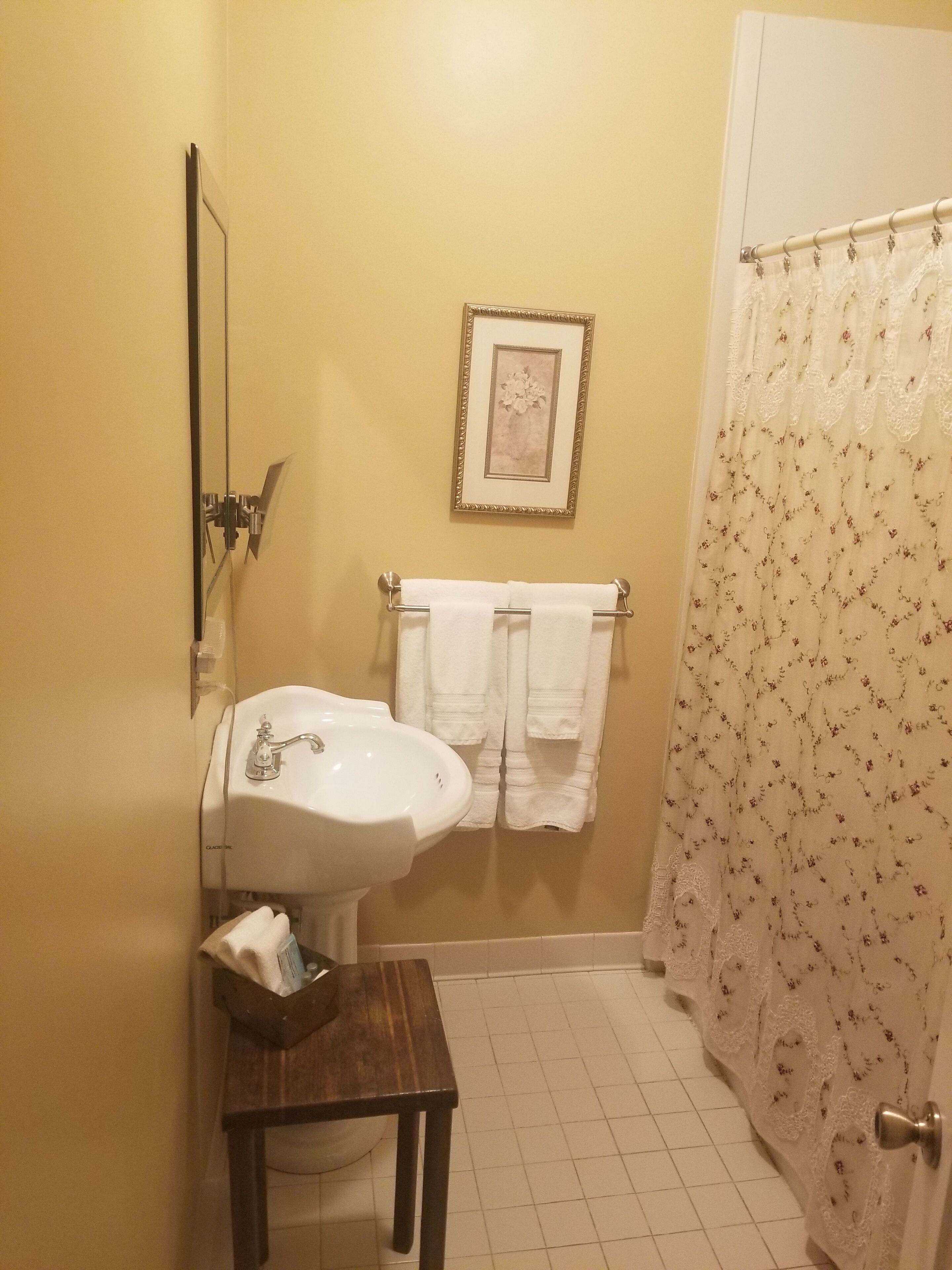 A bathroom with a sink, a framed picture on the wall, a towel rack with towels, and a shower curtain.