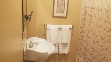 A bathroom with a sink, a framed picture on the wall, a towel rack with towels, and a shower curtain.