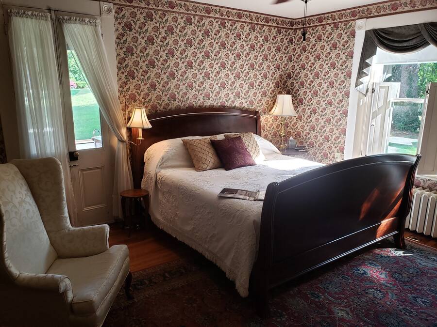 A bedroom with a bed, a chair, a nightstand, a lamp, and a window with curtains.