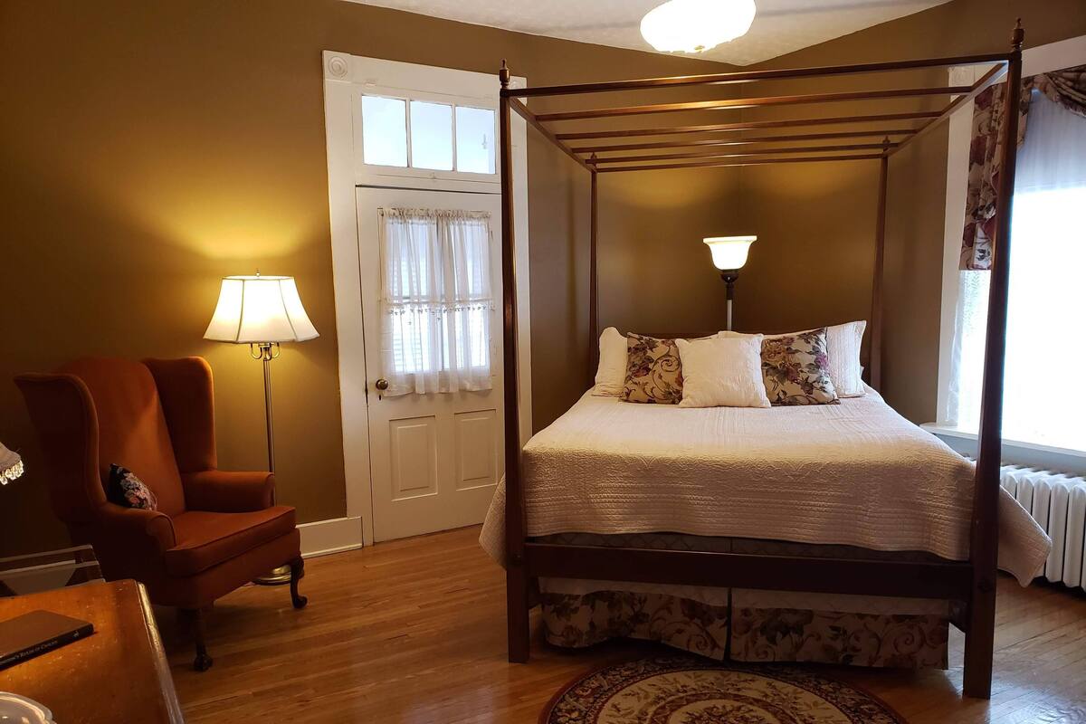 A four-poster bed with a floral bedspread, a round rug, a chair, and a lamp.