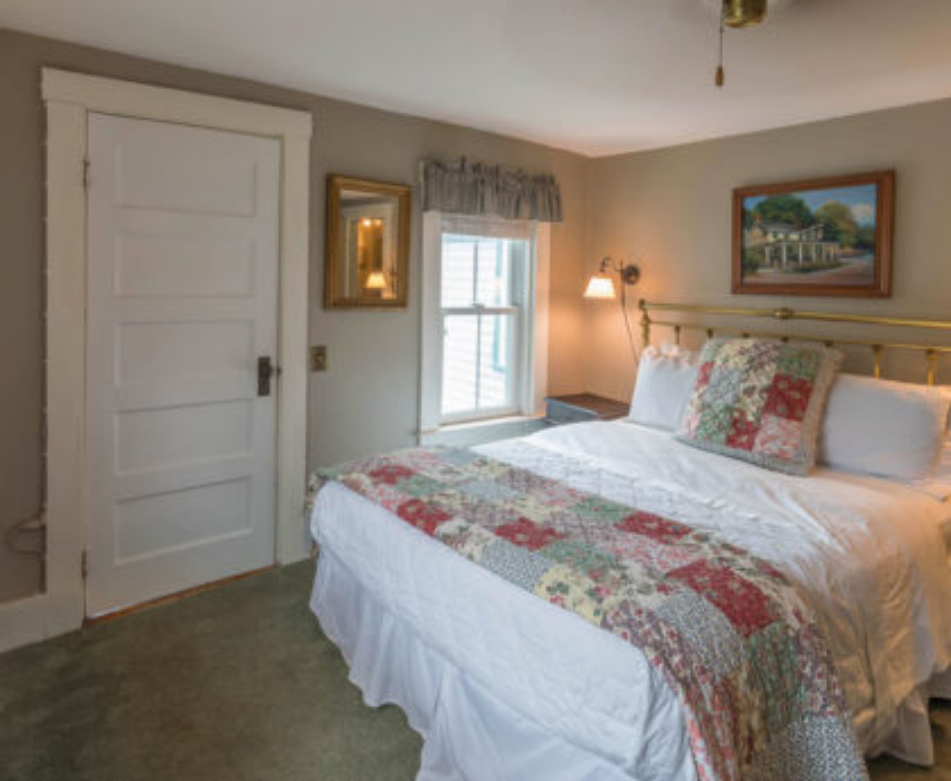 A bedroom with a bed, a door, a window, and a painting on the wall.