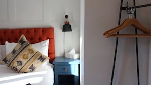 A hotel room with a red upholstered headboard, a bedside table with a lamp, a hanging wooden hanger, and a white door.