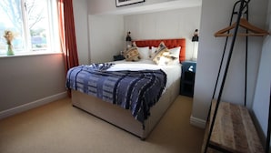 A bedroom with a bed, nightstands, a hanging light, a window with curtains, and a wooden bench.