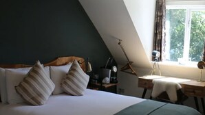 A bedroom with a bed, a desk, a lamp, and a window with curtains. - Nags Head (Great Missenden)
