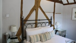 A bedroom with a wooden ceiling structure, a metal bed frame, white bedding, a bedside table with a lamp, and a small bedside table with a tissue box.
