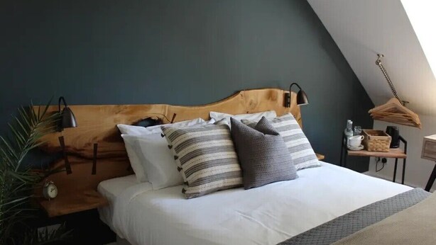 A bedroom with a wooden headboard, a bed with white bedding and striped pillows, a bedside lamp, a small table with a lamp, and a hanging light fixture.