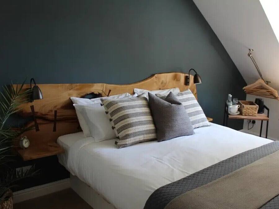 A bedroom with a wooden headboard, a bed with white bedding and striped pillows, a bedside lamp, a small table with a lamp, and a hanging light fixture.