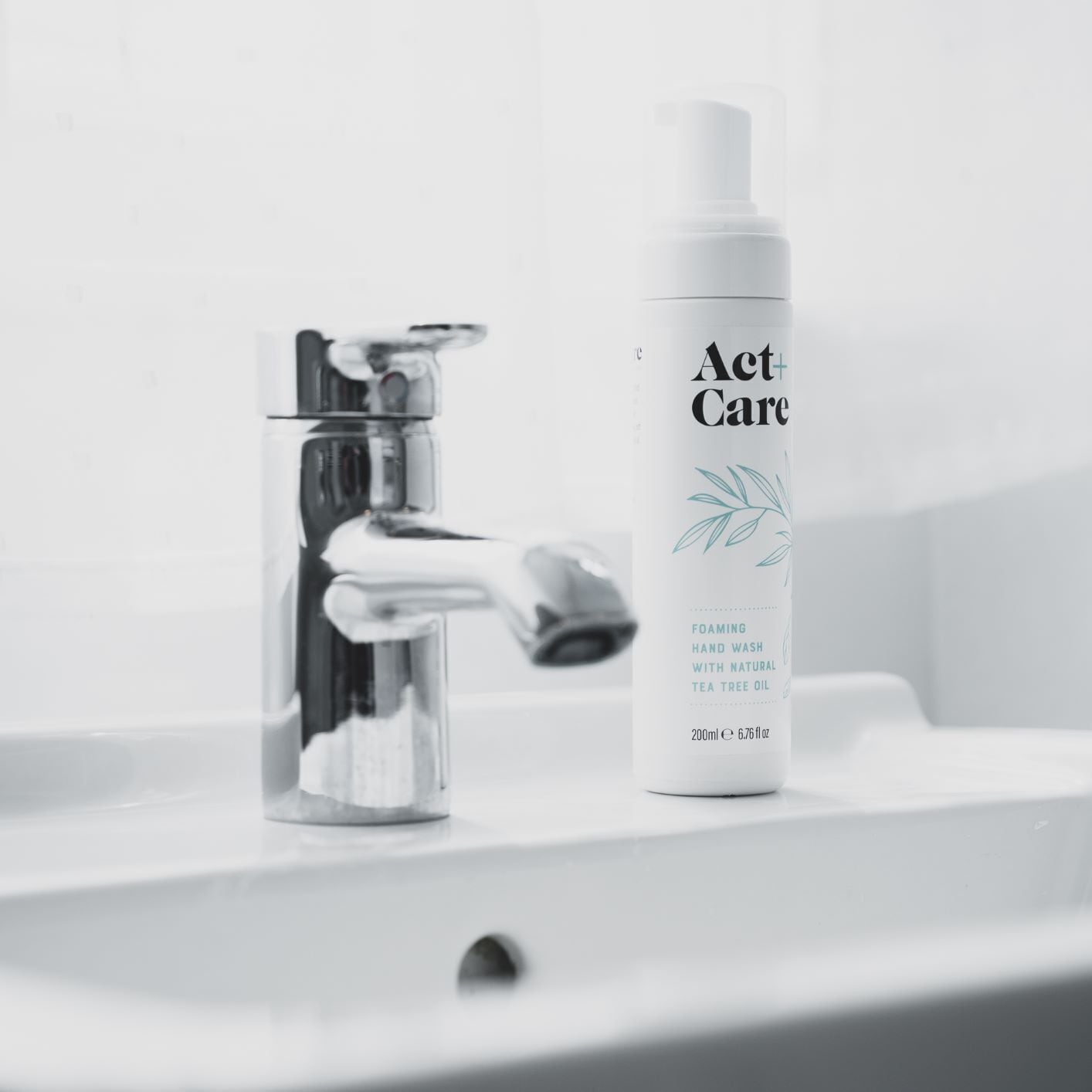 A bathroom sink with a chrome faucet and a bottle of Act+Care hand wash.