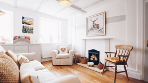 A cozy living room with a fireplace, a sofa, a chair, and artwork on the walls. - The Old Store Guest House (Chichester)