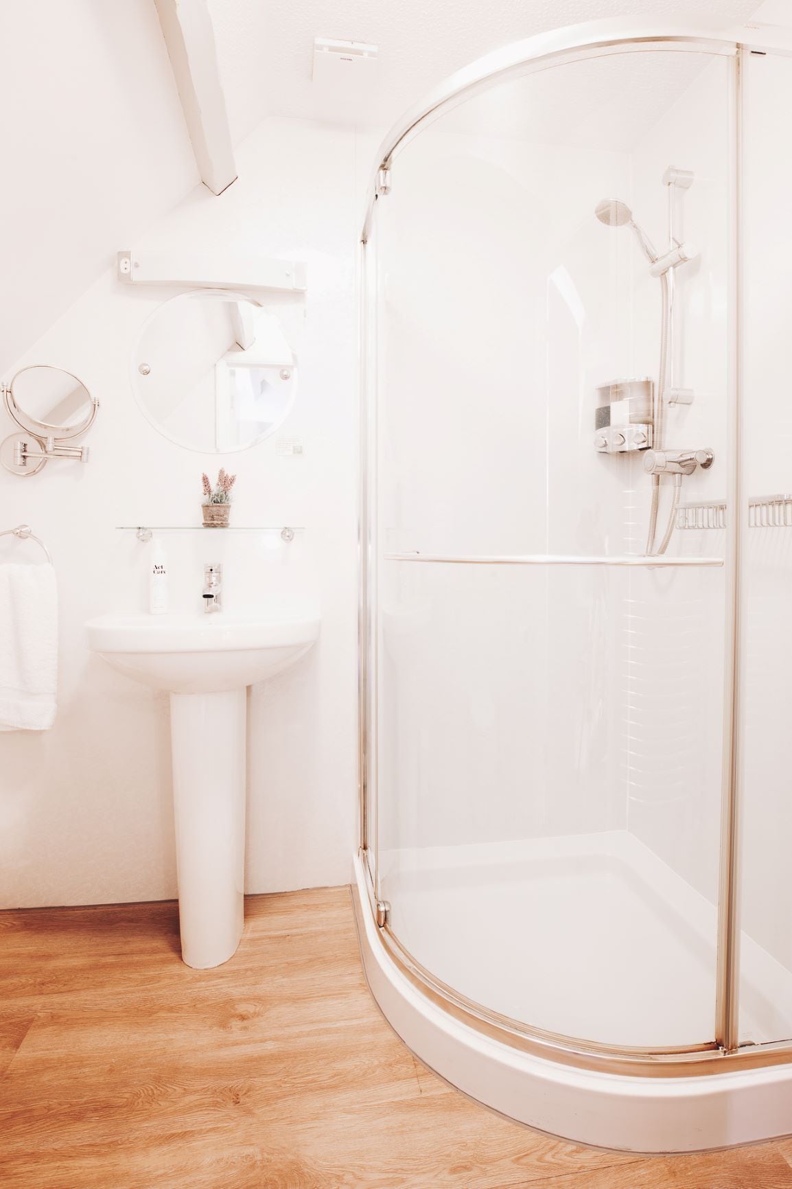 A bathroom with a glass-enclosed shower, a pedestal sink, and a mirror.