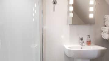 Ein modernes Badezimmer mit einer gläsernen Duschkabine, einem weißen Waschbecken mit Spiegel darüber und einem Handtuchhalter mit gefalteten Handtüchern.